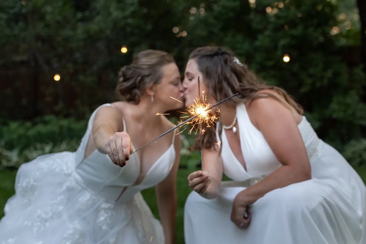 Two brides sharing a kiss over a lit sparkler
