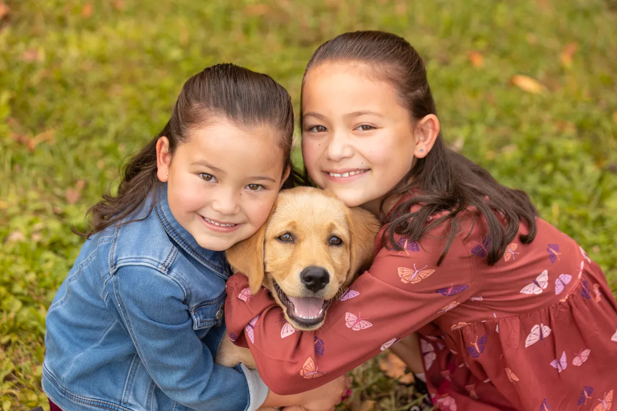 Two sisters hugging a golden retriever puppy between them