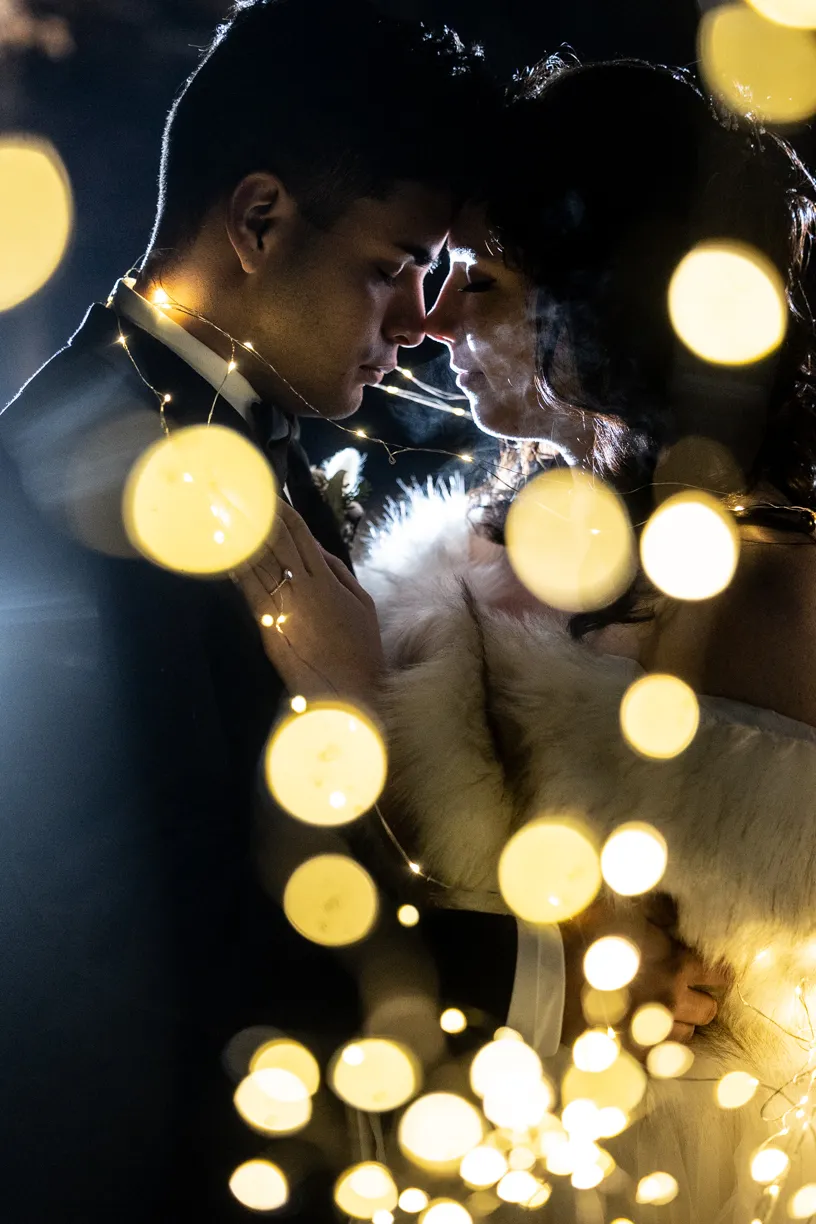 Couple about to kiss behind a blur of string lights
