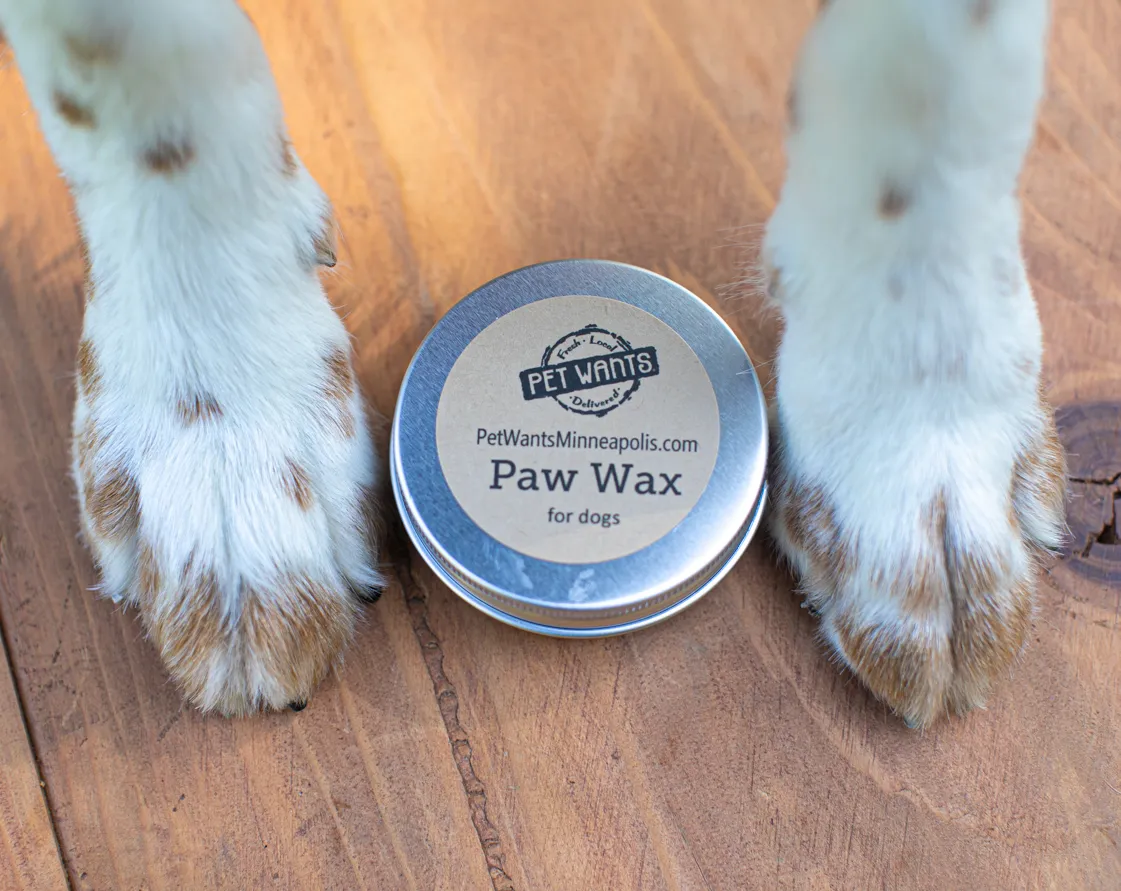 Dog paws on either side of a tin of Pet Wants paw wax