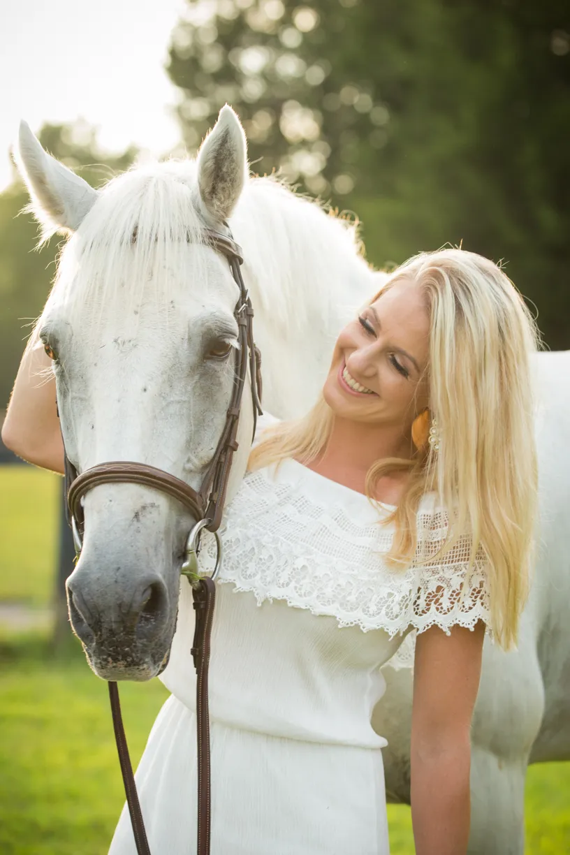 Woman in a white dress smiling beside her white horse