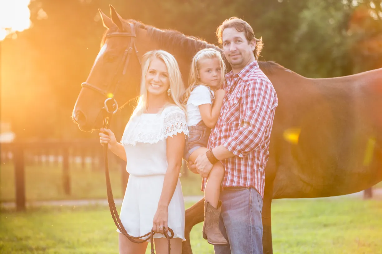 Family with their young daughter and horse at sunset