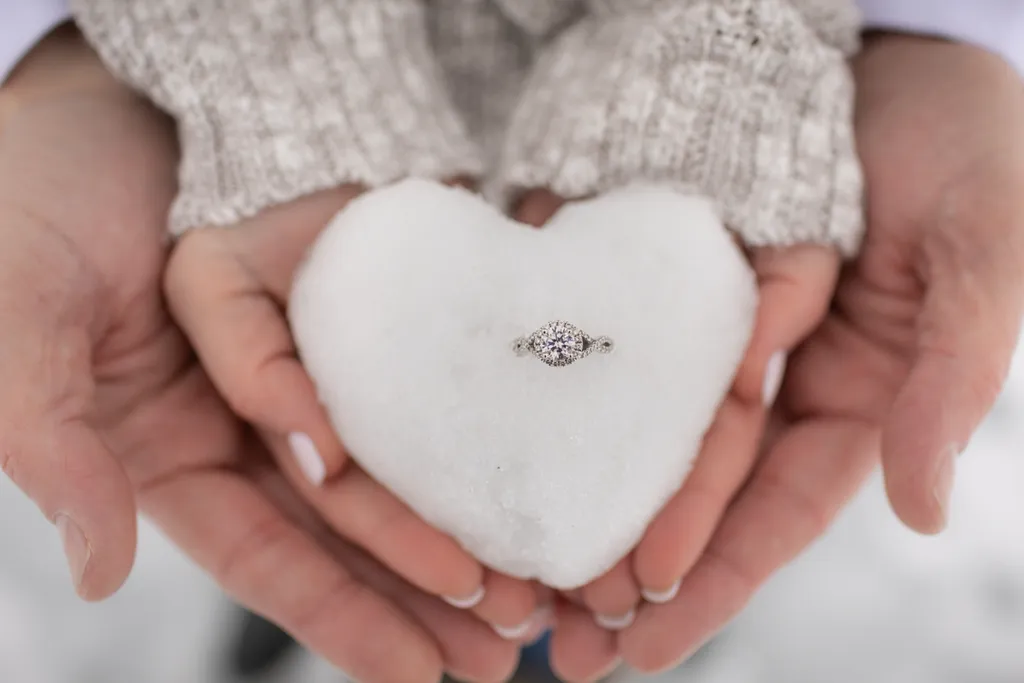 hands holding engagement ring  in heart shaped snowball