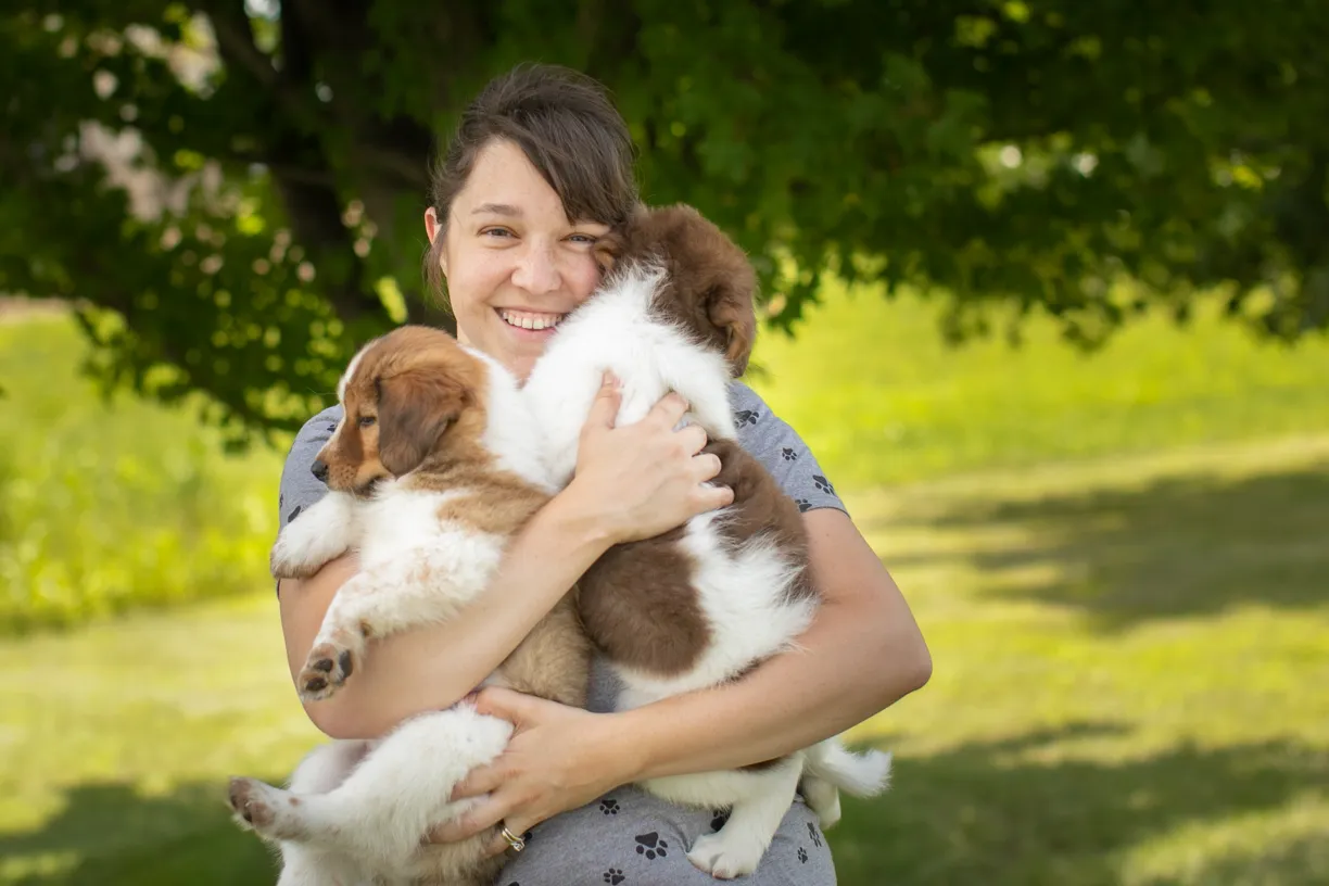 Kelly hugging two fluffy puppies in a park