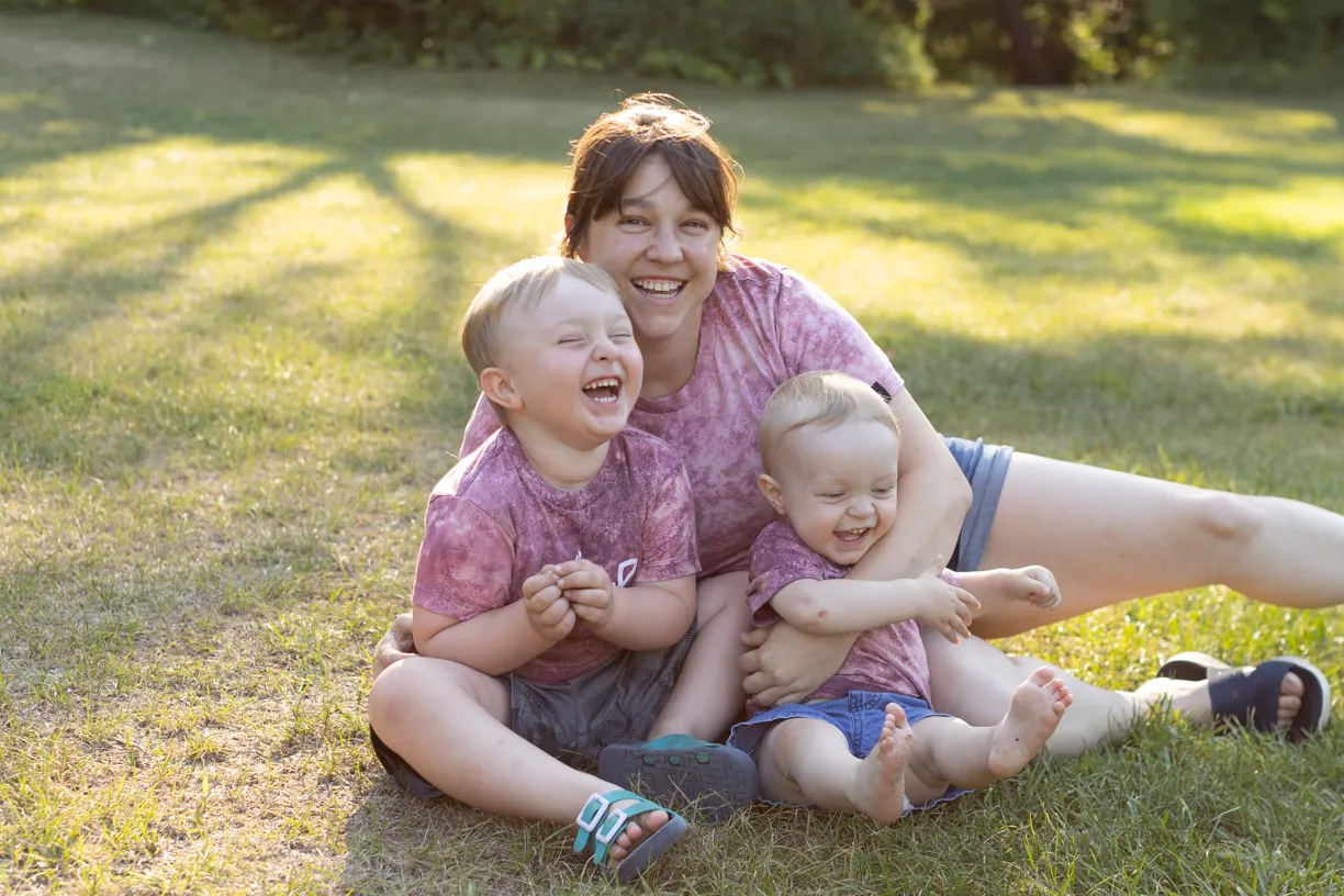 Kelly sitting in the grass with her two young children