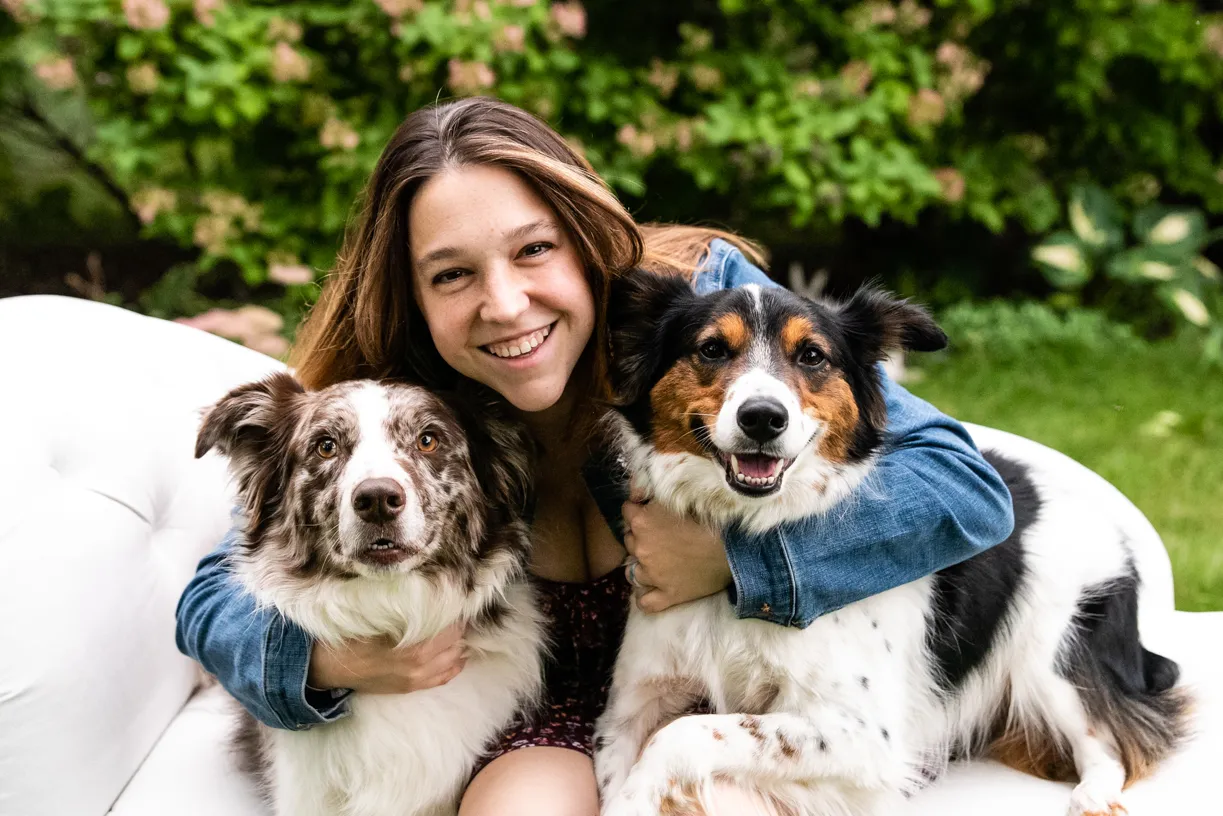 Smiling woman hugging two Australian shepherds in a garden