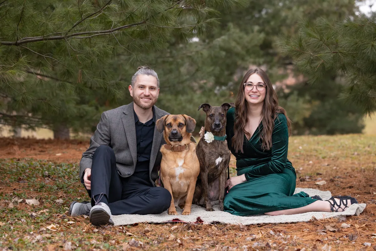 Couple sitting on a blanket in autumn leaves with their two dogs